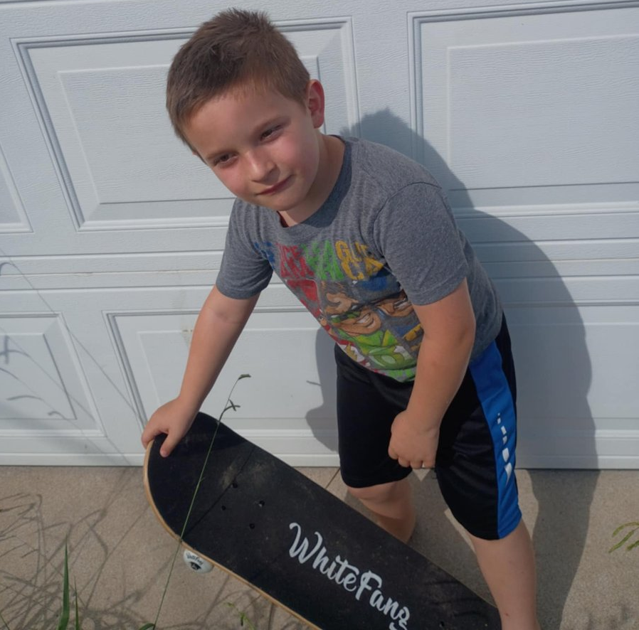 WhiteFang Complete Skateboard Review - Young boy holding WhiteFang skateboard in front of garage door